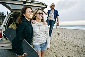 Caucasian friends near car hatch at beach holding skateboards