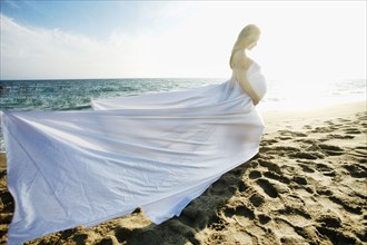 Wind blowing dress of Mixed Race expectant mother at beach
