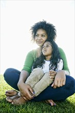 Portrait of pensive mixed race mother and daughter sitting in grass