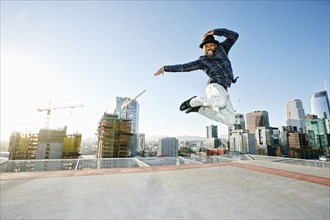 Black man dancing and jumping on urban rooftop