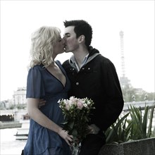 Caucasian woman holding bouquet and kissing boyfriend near Eiffel Tower
