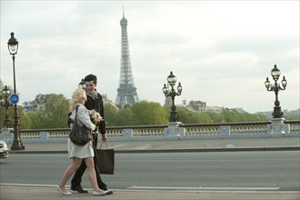 Caucasian couple walking across bridge with Eiffel Tower in background