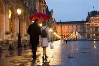 Caucasian couple walking in rain at night at the Louvre