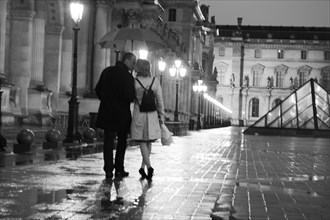 Caucasian couple kissing in rain at night at the Louvre