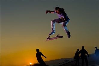 Skateboarder doing stunt in mid-air at sunset