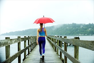 Caucasian woman in sportswear with red umbrella on pier