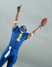Mixed race football player with arms raised holding football