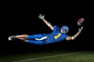 Mixed race football player jumping in mid-air catching football