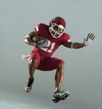 Grimacing Black football player carrying football in mid-air