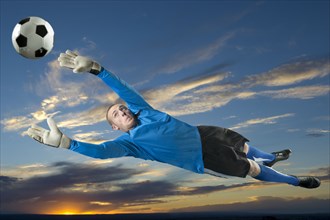 Caucasian soccer goalie jumping in mid-air catching ball