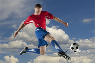 Caucasian soccer player jumping in mid-air kicking ball