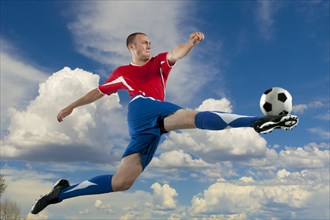 Caucasian soccer player jumping in mid-air kicking ball