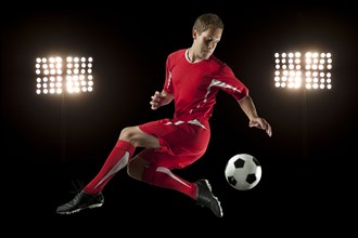 Soccer player jumping in mid-air kicking ball at night