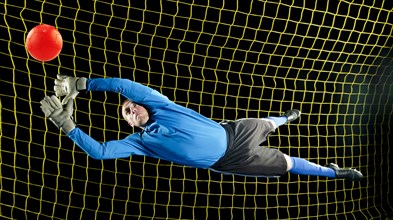 Caucasian soccer goalie jumping in mid-air catching ball at night