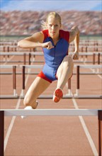 Caucasian runner jumping over hurdles on track