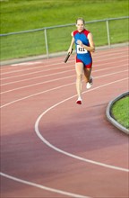 Caucasian runner holding baton running on track