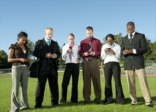 Business people standing in field text messaging on cell phones