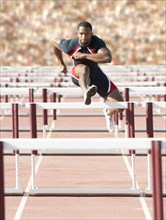 Black runner jumping hurdles in track race