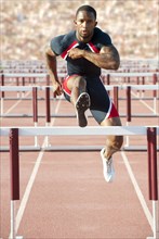 Black runner jumping hurdles in track race
