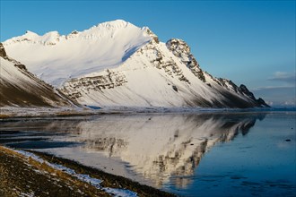 Snowy mountain reflected in still lake in arctic landscape