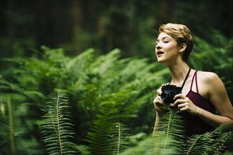 Caucasian woman holding camera in forest