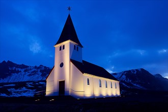 White church illuminated near snowy mountains at night