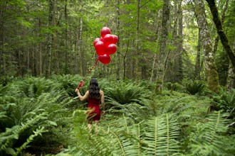 Korean woman holding red balloons in lush forest
