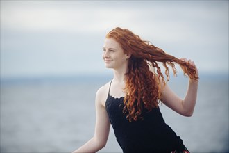 Red haired girl playing with hair on beach