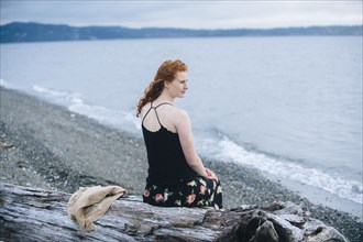Girl sitting on driftwood on beach