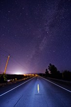 Paved road under starry night sky illuminated by headlights