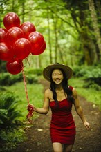 Korean woman carrying red balloons in lush forest