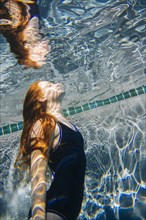 Teenage girl with red hair swimming underwater in pool