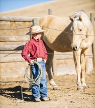 Caucasian boy in cowboy outfit admiring horse on ranch