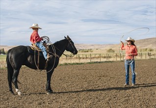 Caucasian woman teaching boy to use lasso on ranch