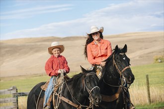 Caucasian mother and son on horseback on grassy hill