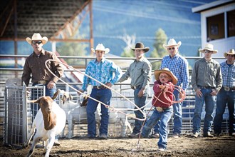 Cowboys teaching boy to lasso goat at rodeo