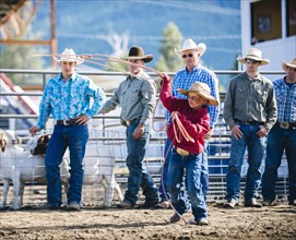 Cowboys watching boy throw lasso in rodeo