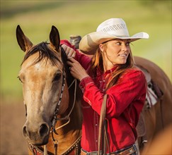 Caucasian cowgirl standing with horse on ranch