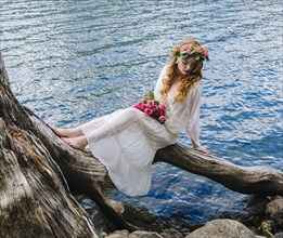Caucasian woman wearing flower crown on log at river