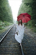 Caucasian woman walking on train tracks with umbrella in forest