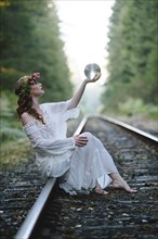 Caucasian woman holding crystal ball on train tracks