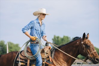 Caucasian cowgirl holding lasso on horseback