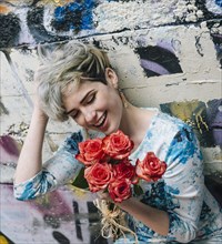 Laughing Caucasian woman at graffiti wall holding flowers