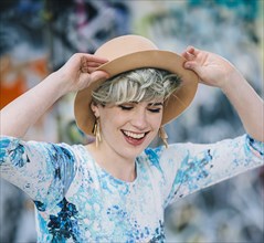 Laughing Caucasian woman holding hat at graffiti wall