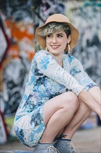 Smiling Caucasian woman crouching at graffiti wall