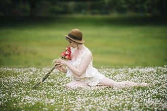 Caucasian woman sitting in field of flowers smelling roses