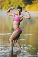 Mixed Race woman flexing muscles in lake