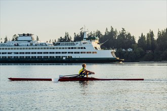 Caucasian man rowing on lake near cruise ship