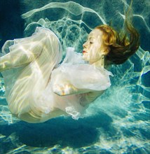 Caucasian woman wearing dress swimming underwater