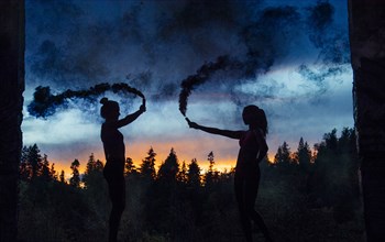 Silhouette of women holding smoking flares